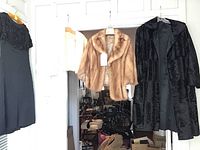 Three garments hanging side by side: black beaded dress, tan mink fur jacket, black textured car coat