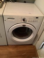 Front view of Frigidaire washer installed next to a dryer, showing control panel and front door.