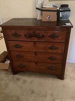 Front view of the vintage wooden dresser showing four drawers with decorative metal handles and locks.