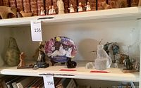 Wide shelf view showing crystal cat statues, animal figurines, decorative cat plate, stone seal and other items
