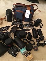 Overview of cameras, lenses, bags, binoculars and accessories arranged on floor