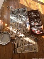 Overview of entire lot laid out on wooden floor: coffee service, flatware on cloths, wooden trays of utensils.