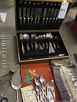 Full view of wooden flatware case open showing sterling and silver plated pieces alongside cloth rolls.