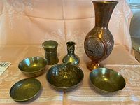 Full view of all items in the lot including copper vase, small brass pot and vase, and four brass bowls on fabric background