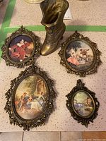 Four ornate brass framed miniature prints and a brass decorative boot arranged on table surface