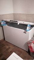 Philco chest freezer in a tiled basement corner with the lid open, showing interior wire baskets and lid support.