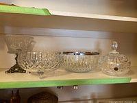 Four cut glass crystal bowls displayed on a shelf, showing various sizes and designs including one with a lid and one with a metal base.