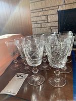 Group of 16 crystal stemware glasses including sherry and white wine glasses, displaying etched starburst and leaf patterns on a wooden surface.