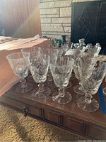 Multiple pinwheel crystal wine and aperitif glasses arranged on a wooden surface, showing 16 glasses in total with intricate cut patterns.