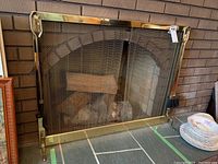 Full view of the metal fireplace screen with brass finish and mesh center in front of a brick fireplace.