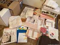 Overview of all linens in lot showing packaged tablecloth, folded towels, doilies, and napkins