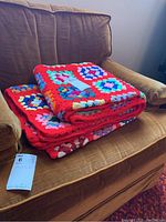 Folded colorful crocheted blanket placed on a brown upholstery chair with a note on top and a measurement tag nearby.