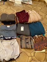 Photo of folded ladies sweaters and tops in various colors and patterns laid on floor showing texture and style variety.