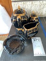 Full view of black glass teapot and creamer with gold trim, alongside black glass ashtray with bubble details.