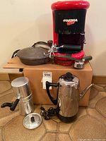 Full view of all items in the lot: red Farma Ciao espresso maker, large cast iron lid, aluminum stovetop coffee roaster, and stainless steel electric coffee pot