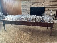Full length photo of midcentury wooden coffee table with glassware on top, showing detailed side panels and tapered legs.