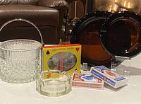 Photo of all items: ice bucket, sealed and unsealed twin deck playing cards, large and smaller smoked glass ashtrays on table