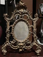 Front view of ornate brass easel stand photo frame with oval photo opening.
