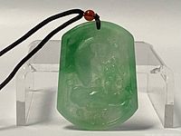 Front view of the green carved jade pendant showing detailed carving and attached black cord with small brown bead.