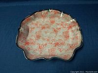 Front and angled view of the hand-painted pottery dish showing scalloped edges and floral design.