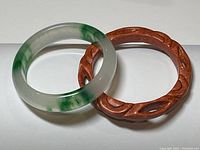 Two bangle bracelets placed side by side, one jade with green coloring and one brown carved.