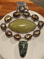 Front view of the vintage sterling silver brooch showing central green gemstone, surrounding baroque pearls, and bottom turquoise stone.