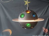 Space age pendant light hanging with lit interior showing colored lenses and acrylic disk around sphere.
