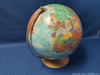 Globe showing Europe, Africa, and parts of Asia with countries in varied colors, mounted on beige base and brown metal meridian.