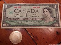 1967 Canadian Centennial one dollar banknote alongside the commemorative one dollar coin on a wooden surface
