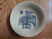 Top view of round pottery bowl showing centered stylized Thunderbird Dancer design in black paint over tan clay surface, highlighting condition and detail.