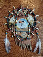 Full view of the dream catcher showing cultured stone centerpiece with eagle painting, carved feathers and bone-like spikes, colorful beads, and hanging white and black-spotted feathers.