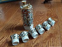 Full set of Kutani porcelain sake container and six matching cups with gold crane designs laid out on wood floor.