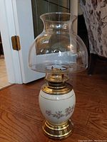Hurricane lamp fully assembled showing porcelain base with floral design, brass burner and base, and clear glass chimney on top.