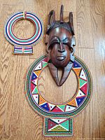 Photo of two vintage African beaded leather necklaces and a hand sculpted wooden mask laid on wood floor to show size and detail.