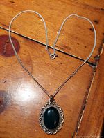 Full view of the necklace and pendant laid flat on a wooden surface, showing chain and pendant details