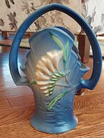 Front angled side view of the blue Roseville Freesia basket vase showing detail of the freesia flower and handle.