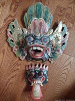 Top view photo showing both colorful vintage Indonesian wooden deity masks on hardwood floor.