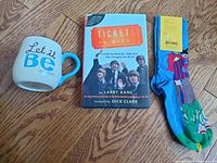 Lot contents with Beatles Ticket to Ride novel, Hallmark Let it Be mug, and Happy Socks on wood floor.