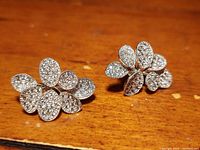 Front view of one earring showing intricate leaf design studded with clear crystals on a textured silver base.