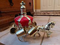 Close-up image of brass horse carriage decanter with porcelain crown stopper and hanging brass mugs