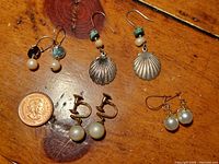 Four pairs of vintage earrings including cultured pearl, gold plated, and natural pearl clamshell styles arranged with a coin for size reference.
