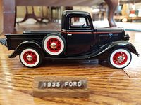 Side view of the black 1935 Ford Pickup scale model with red and white tires and display plaque.