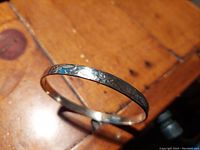 Photo of the hammered sterling silver bracelet placed on a wooden surface, showing the textured surface and circular shape.