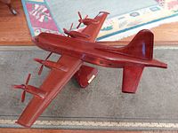 Side angled view of a polished hardwood model airplane with four engines and propellers, shows overall design and form.