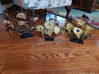 Three vintage wooden ship models displayed on a hardwood floor, showing size relation and overall condition.