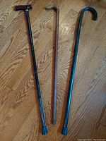 Top view photo showing all three walking canes on hardwood floor, highlighting the wood grain canes and the black metal adjustable cane.