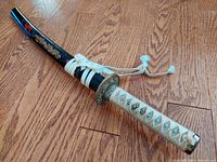 Full view of katana in scabbard laid on hardwood floor