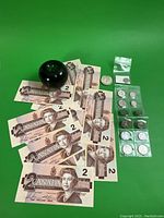 Overview of 14 banknotes, silver dollar, dimes and nickels laid out on green background with reference sphere