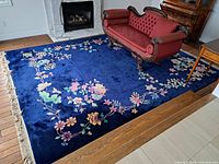 Full view of the navy blue rug laid out in a living room under a red upholstered settee and in front of a fireplace.