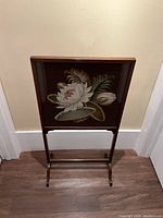 Full view of the antique English fire screen showing wooden frame and needlepoint floral design with dark background.